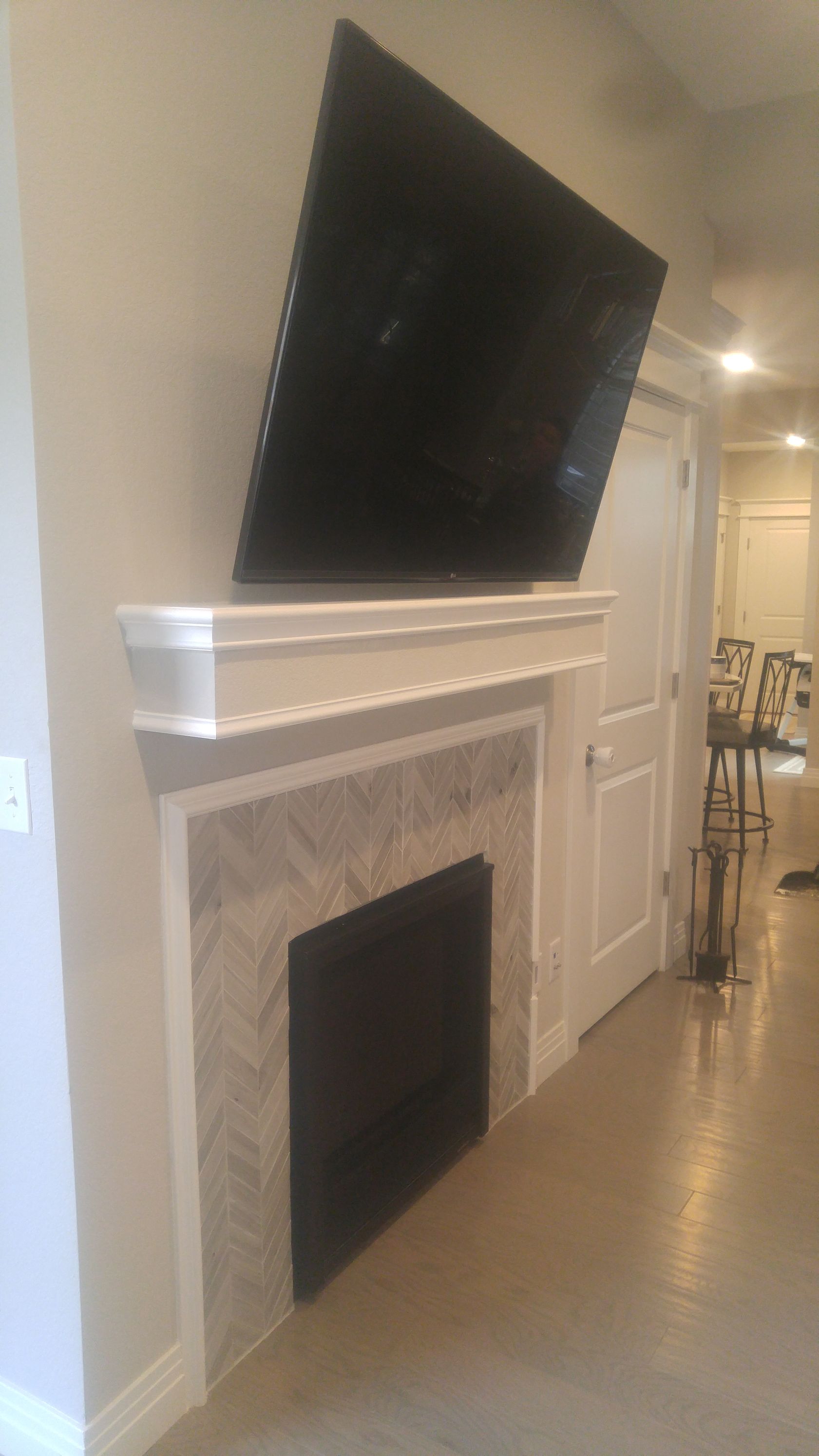 TV mounted above a fireplace with herringbone tile surround, white trim, and a hallway in the background.