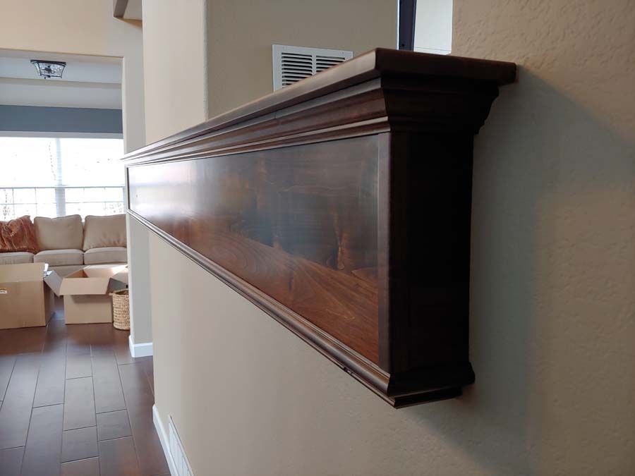 Dark wood wall-mounted shelf with decorative molding, installed on a beige wall in a hallway.