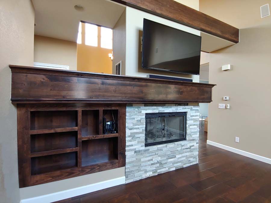Fireplace with stacked stone facade, built-in shelves, dark wood mantel, and mounted TV.