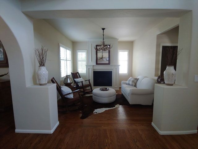Living room with fireplace, white sofa, rocking chairs, and archway with vases on pillars.