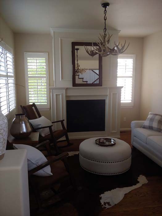 Living room with fireplace, white walls, leather rug, ottoman, chandelier, and sofa.