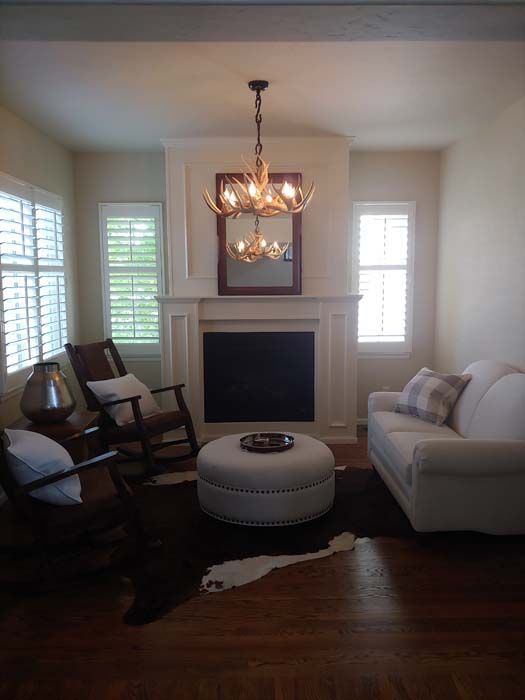 Living room with fireplace, white sofa, rocking chairs, antler chandelier, and shutters.