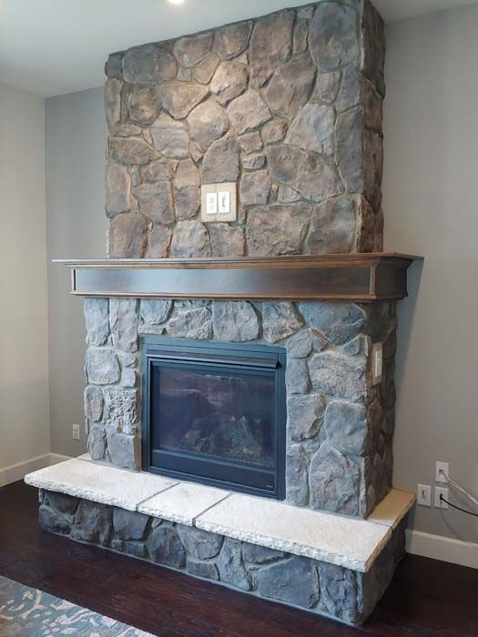 Stone fireplace with dark wood mantel and light-colored hearth against a gray wall.