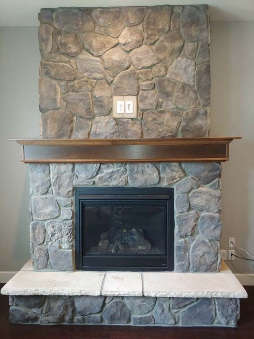 Stone fireplace with wooden mantle and light switches.