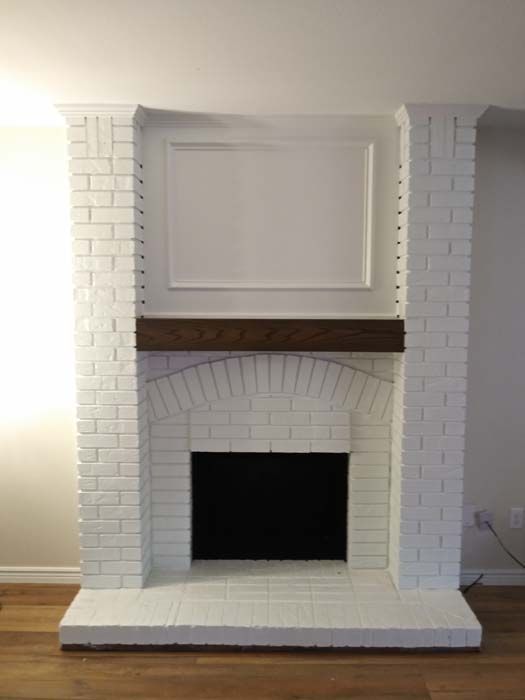 White brick fireplace with a dark wooden mantel and black fireplace opening.