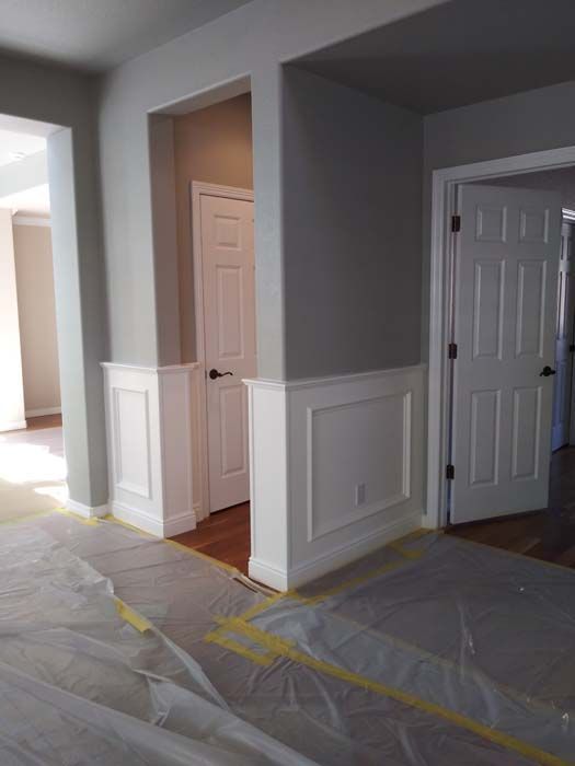 Interior view of a room with wainscoting and two white doors. Walls are painted gray. Plastic sheeting on floor.