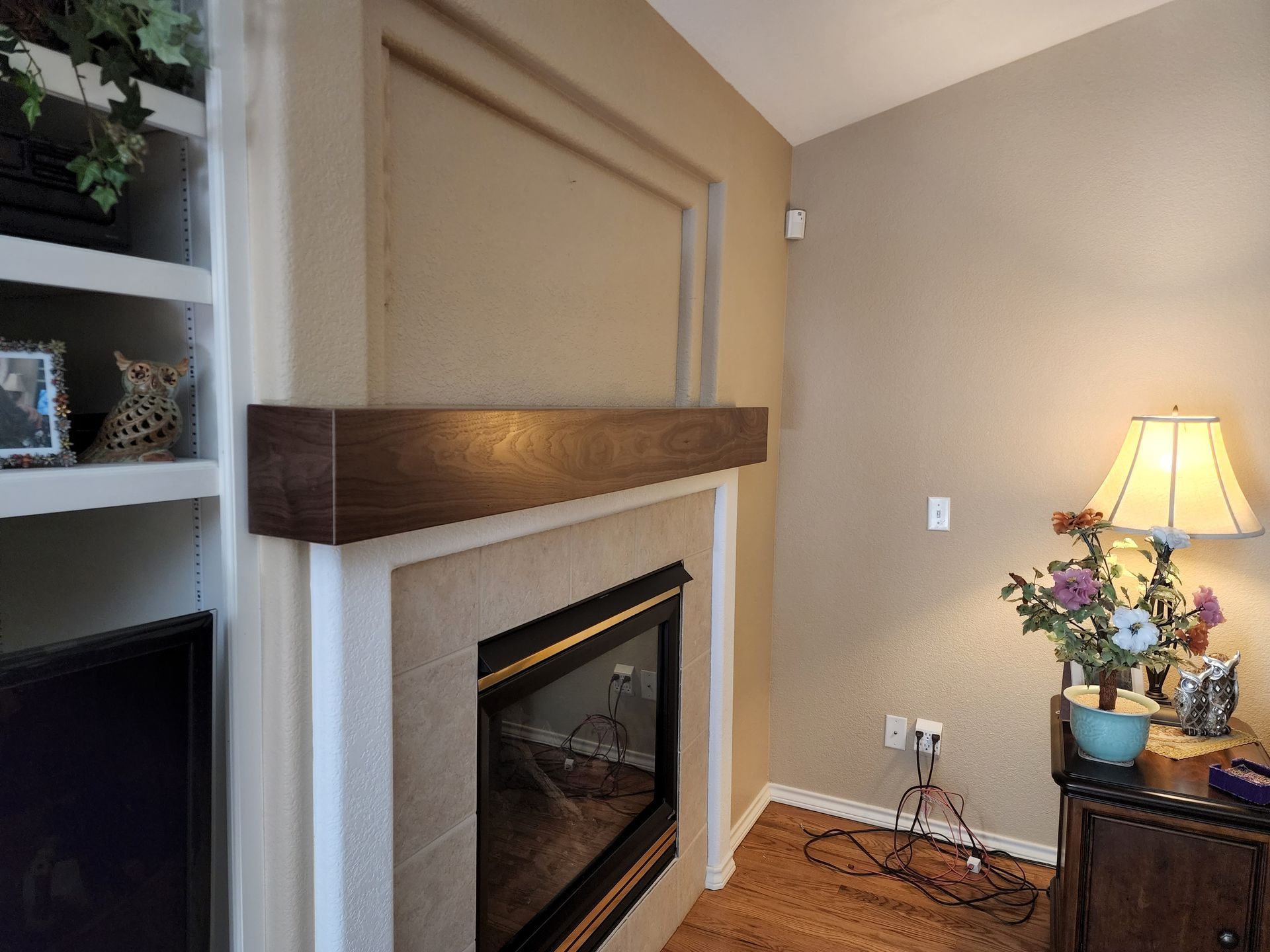 Fireplace with dark wooden mantel, built-in shelving, and a lamp on a side table.