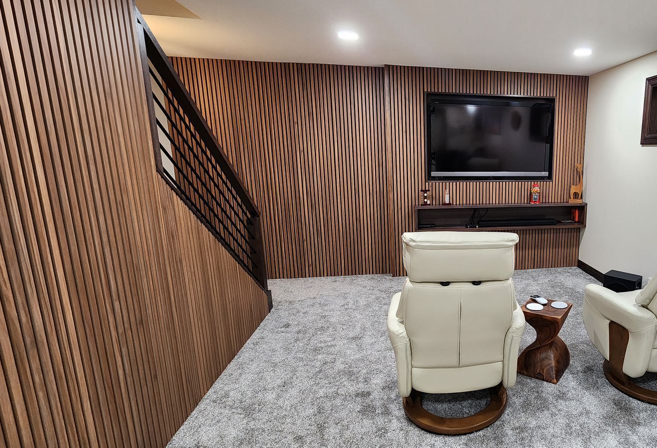 Cozy home theater with wooden accent walls, mounted TV, recliner chairs, and gray carpet. Staircase on the left.