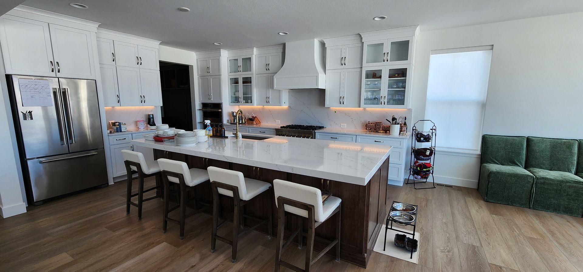 Modern kitchen with white cabinets, large island, stainless steel appliances, and a green sofa.