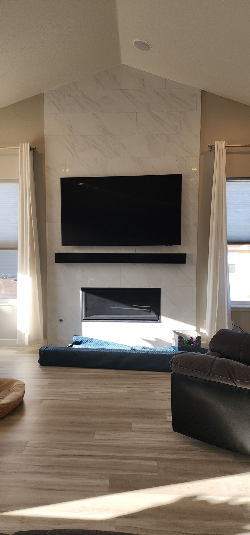 Living room with fireplace, TV, and soundbar on a marble wall. The fireplace is filled with blue stones.