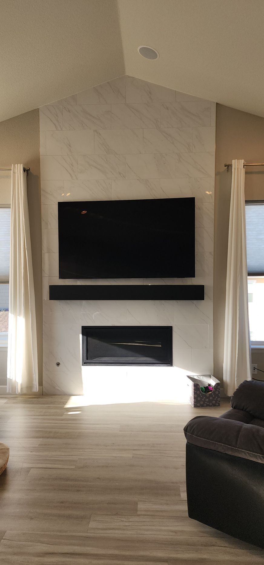 Living room with a wall-mounted TV, fireplace, and tall windows letting in bright daylight