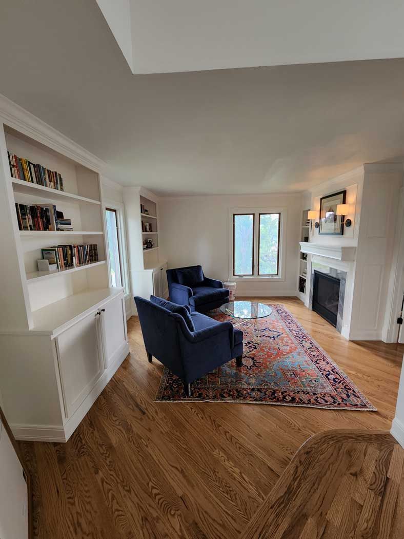 Living room with hardwood floors, built-in bookshelves, blue armchairs, and a fireplace.