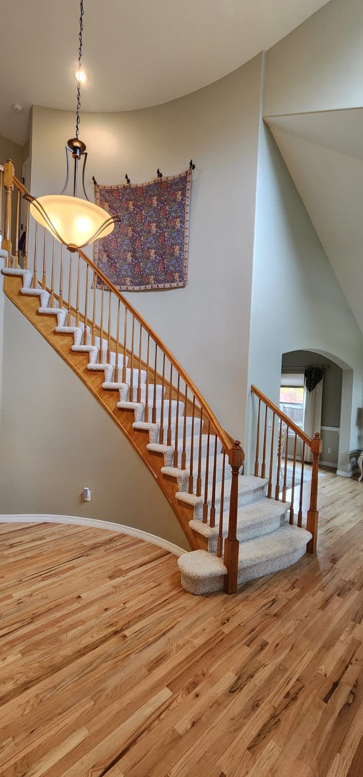 Interior view of a staircase with hardwood floors, white balusters, and a colorful wall hanging.