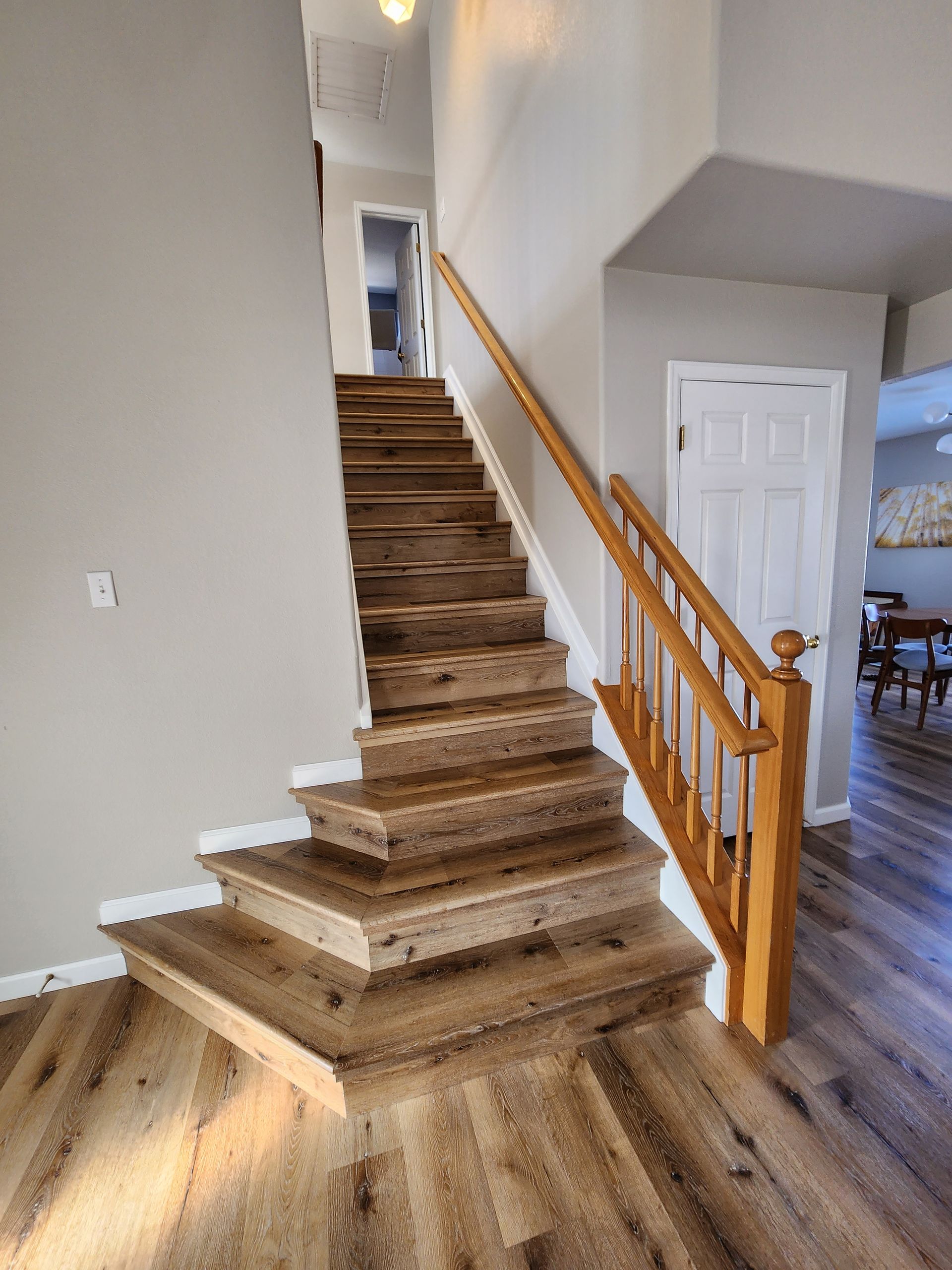 Wooden staircase leading to a hallway. Light brown wood, tan walls, and a white door are visible.