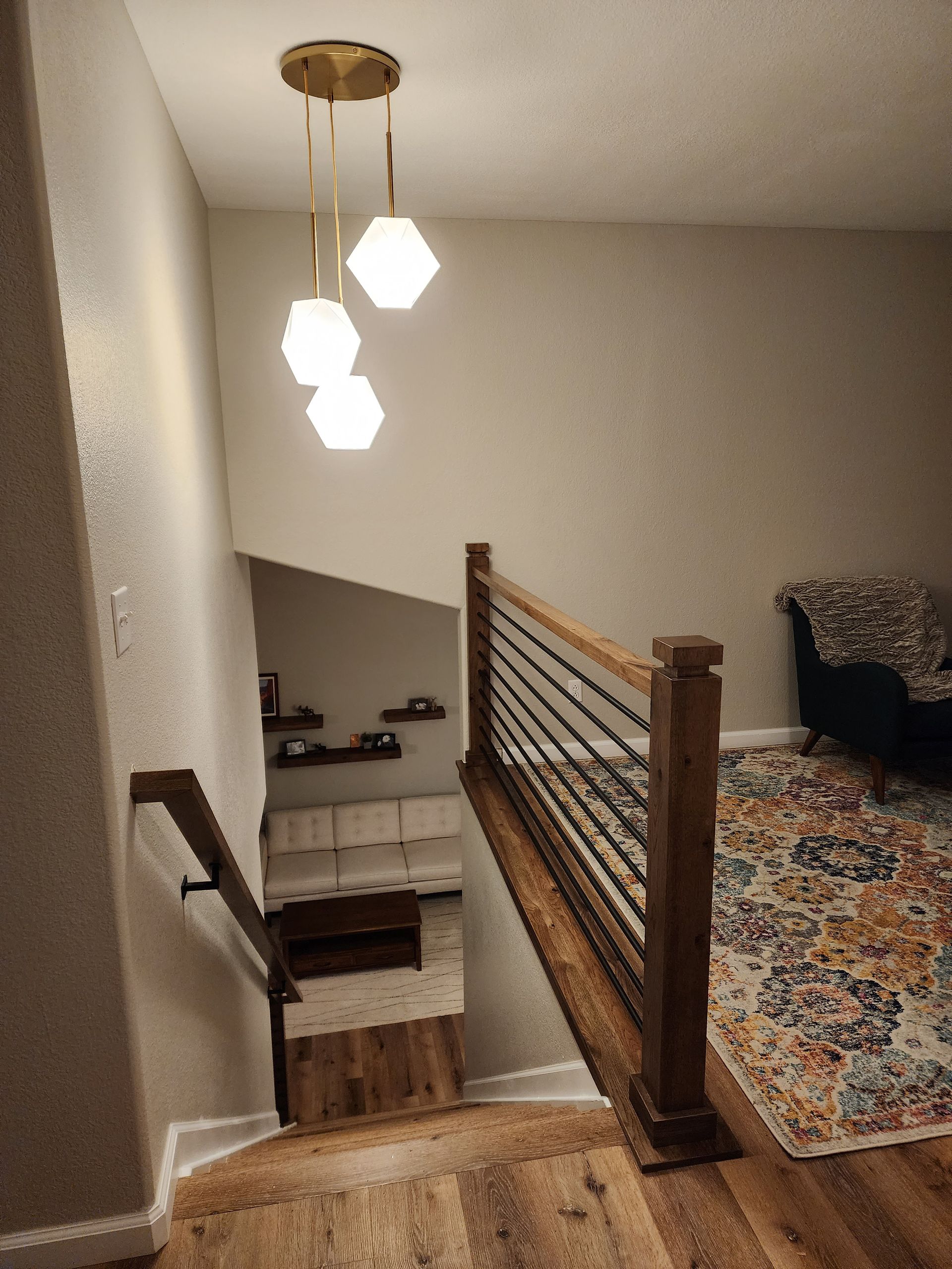 Stairwell with wood railing, hexagonal pendant lights, and a patterned rug.