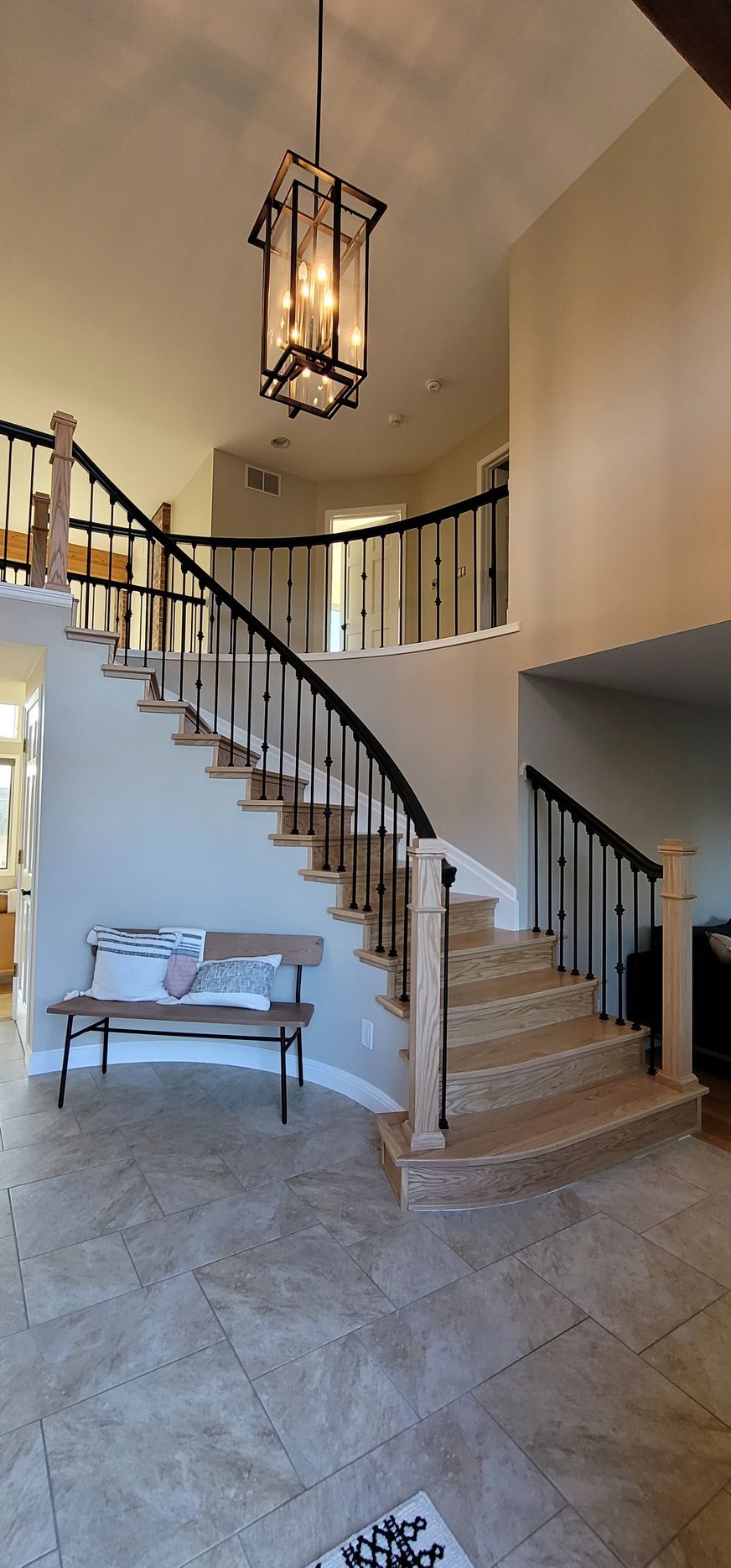 An elegant foyer with a curved staircase, chandelier, and a small wooden bench.