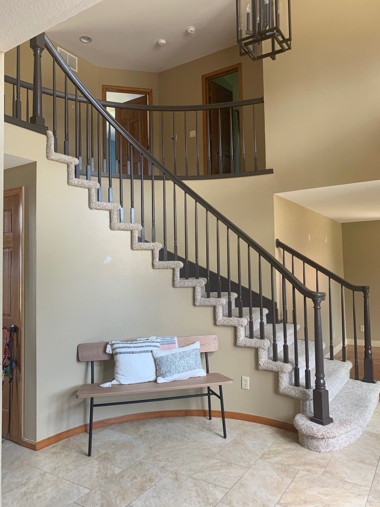 A staircase with dark railings, carpeted steps, and a bench with pillows; neutral-toned walls.