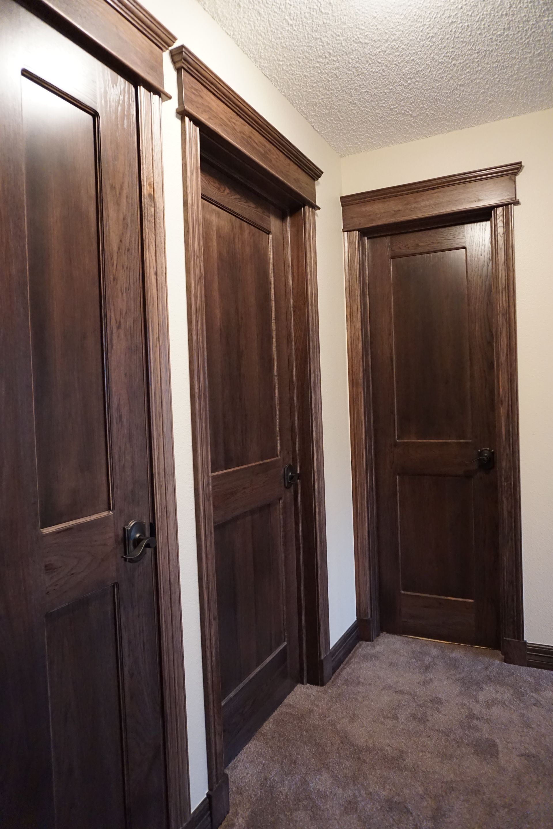 Three dark-stained wooden doors with decorative trim, set against beige walls and a brown carpet.