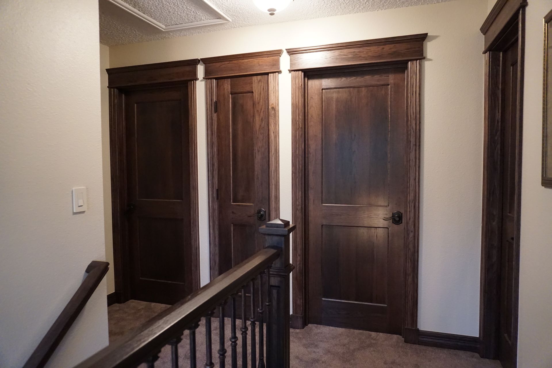 Hallway with three dark wood doors, brown carpet, and a wooden banister.