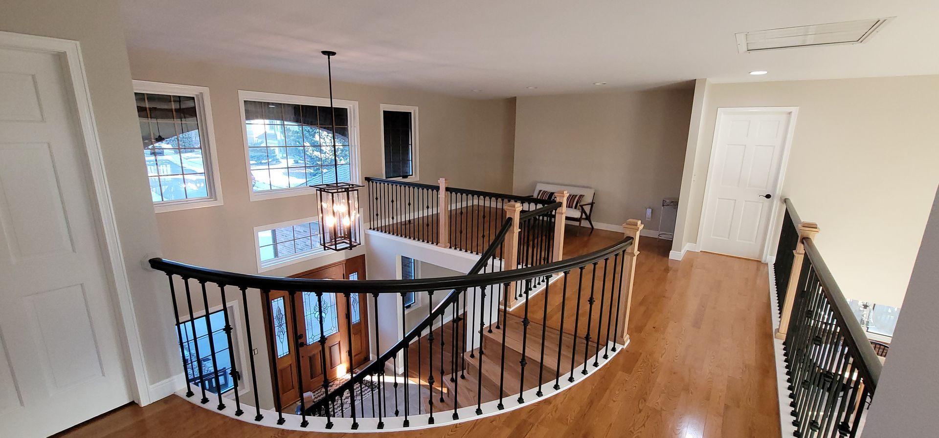 Interior view of a curved staircase with a black railing, wooden floor, and neutral walls.