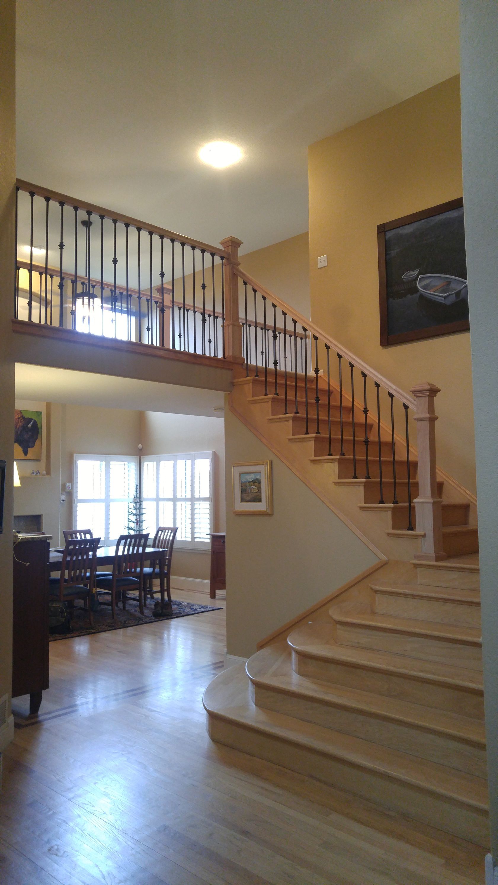 Interior view of a staircase and a mezzanine, with wooden banisters, and a dining room visible.