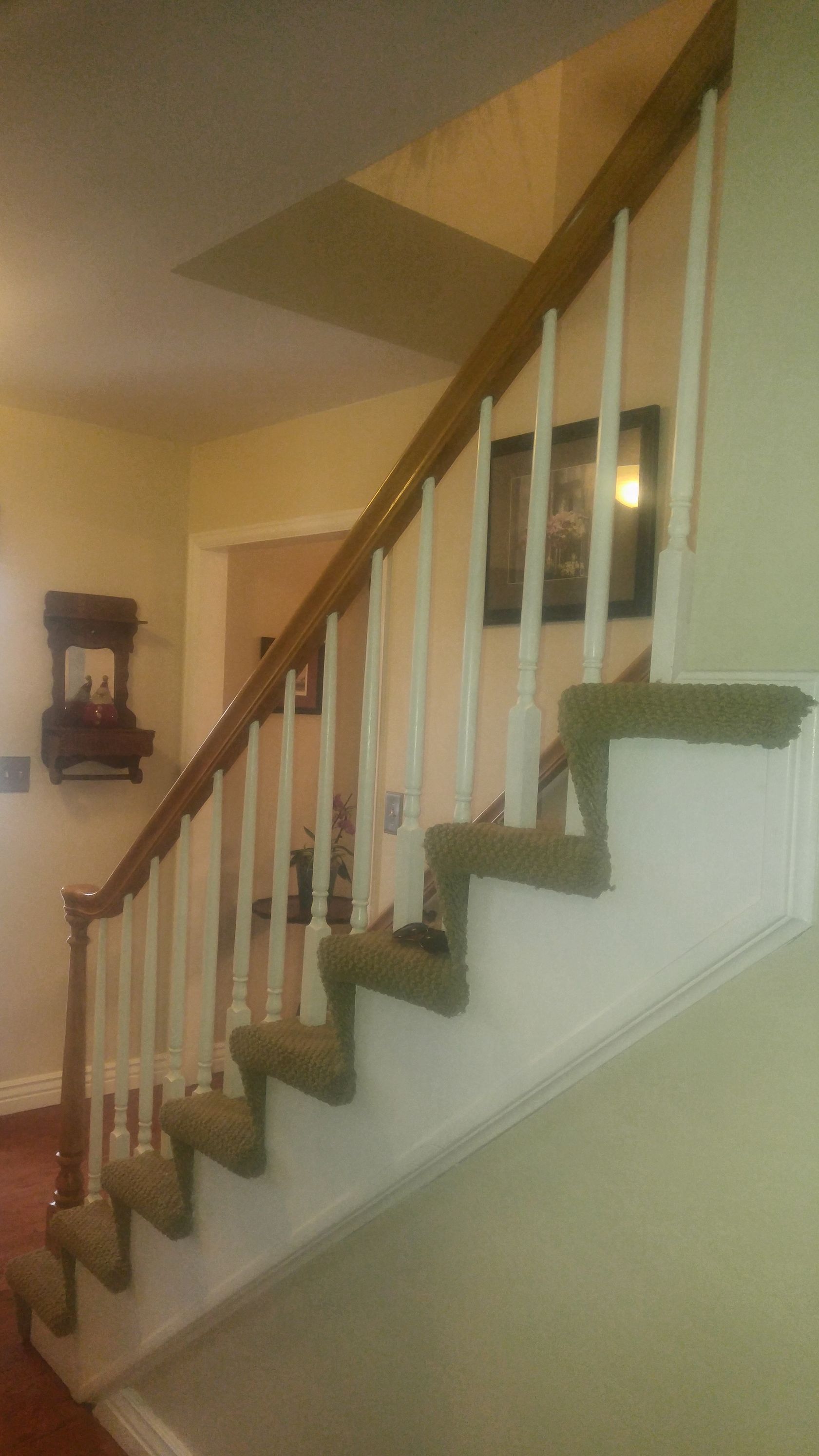 Staircase with wooden handrail and white spindles; green carpet on steps.