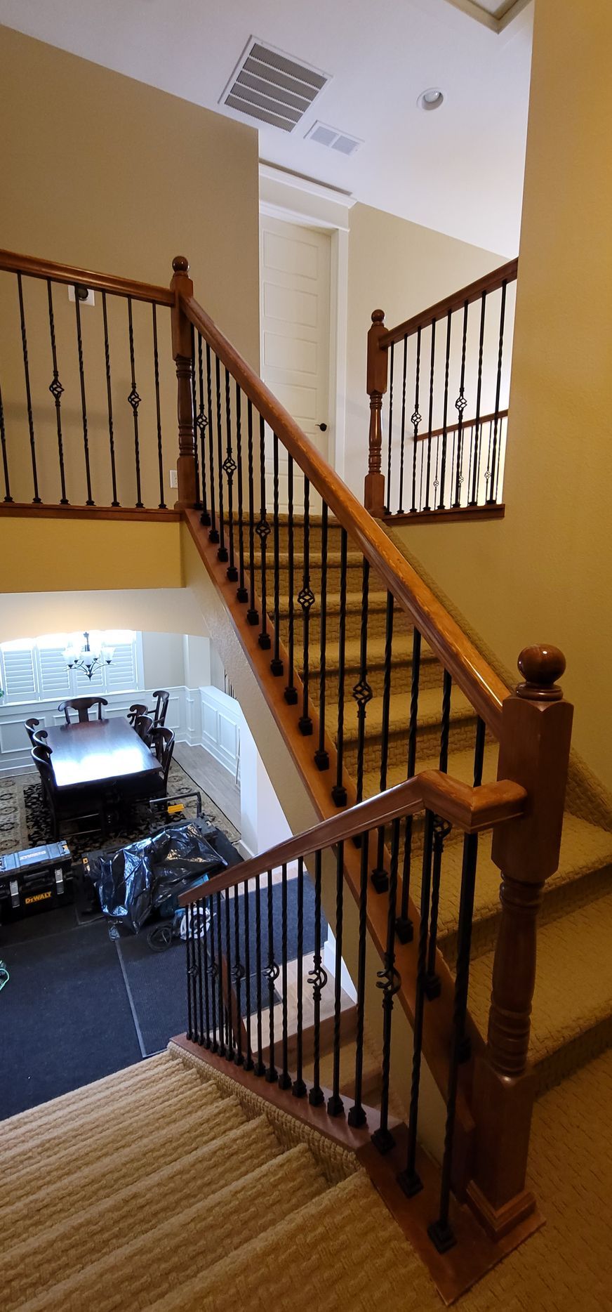 Staircase with wooden railings and black vertical bars. View from the top floor to the ground floor with a dining table.