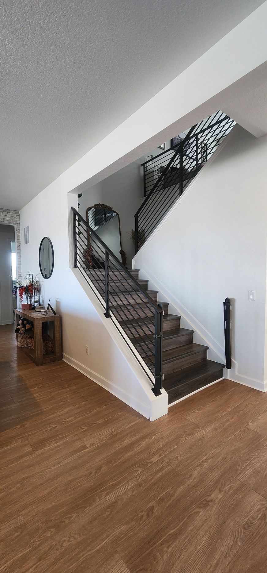 Interior view of a modern staircase with dark metal railings, white walls, and wood-look flooring.