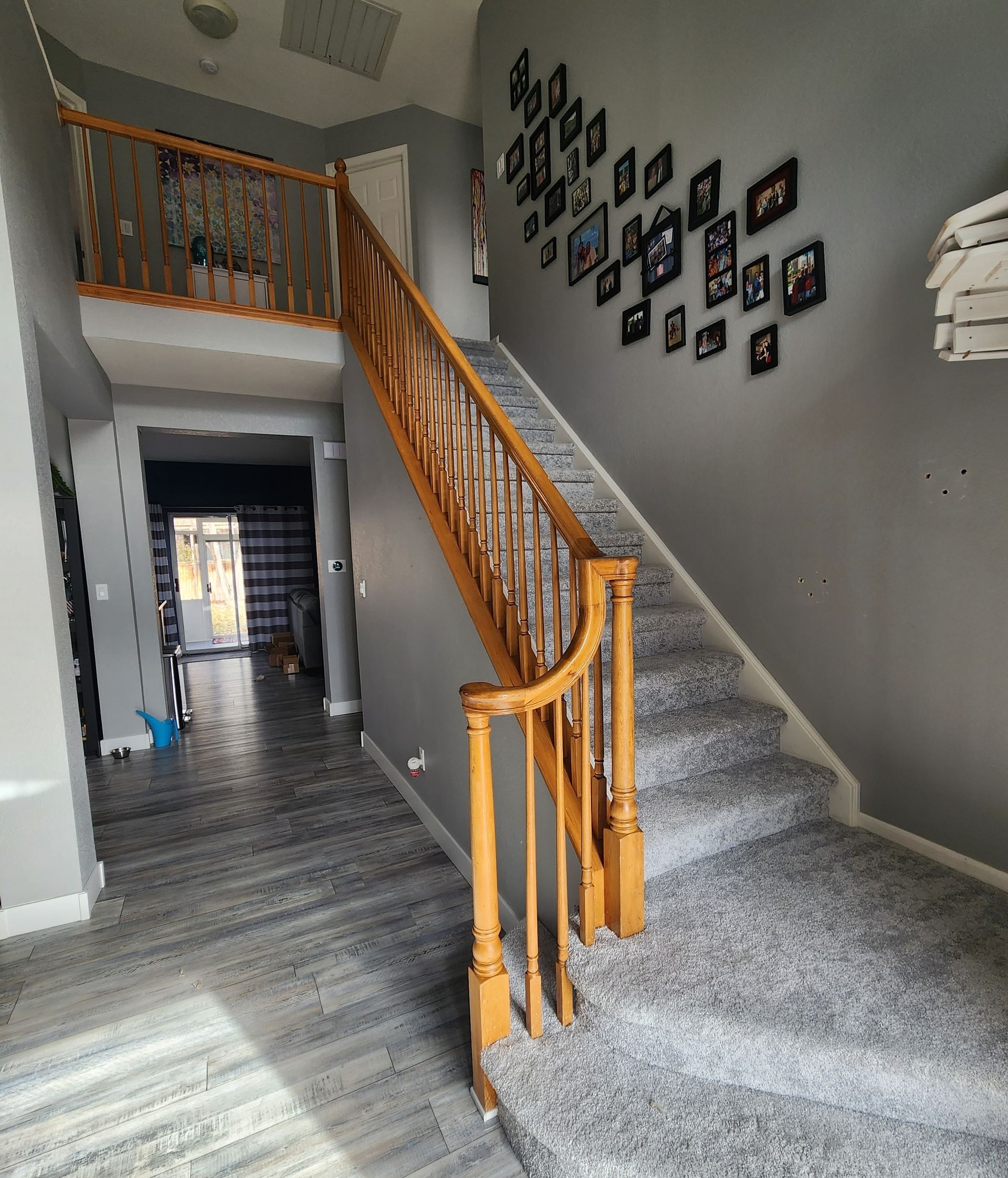Gray carpeted staircase with wood banister ascends to a second floor. Grey walls, dark framed photos.