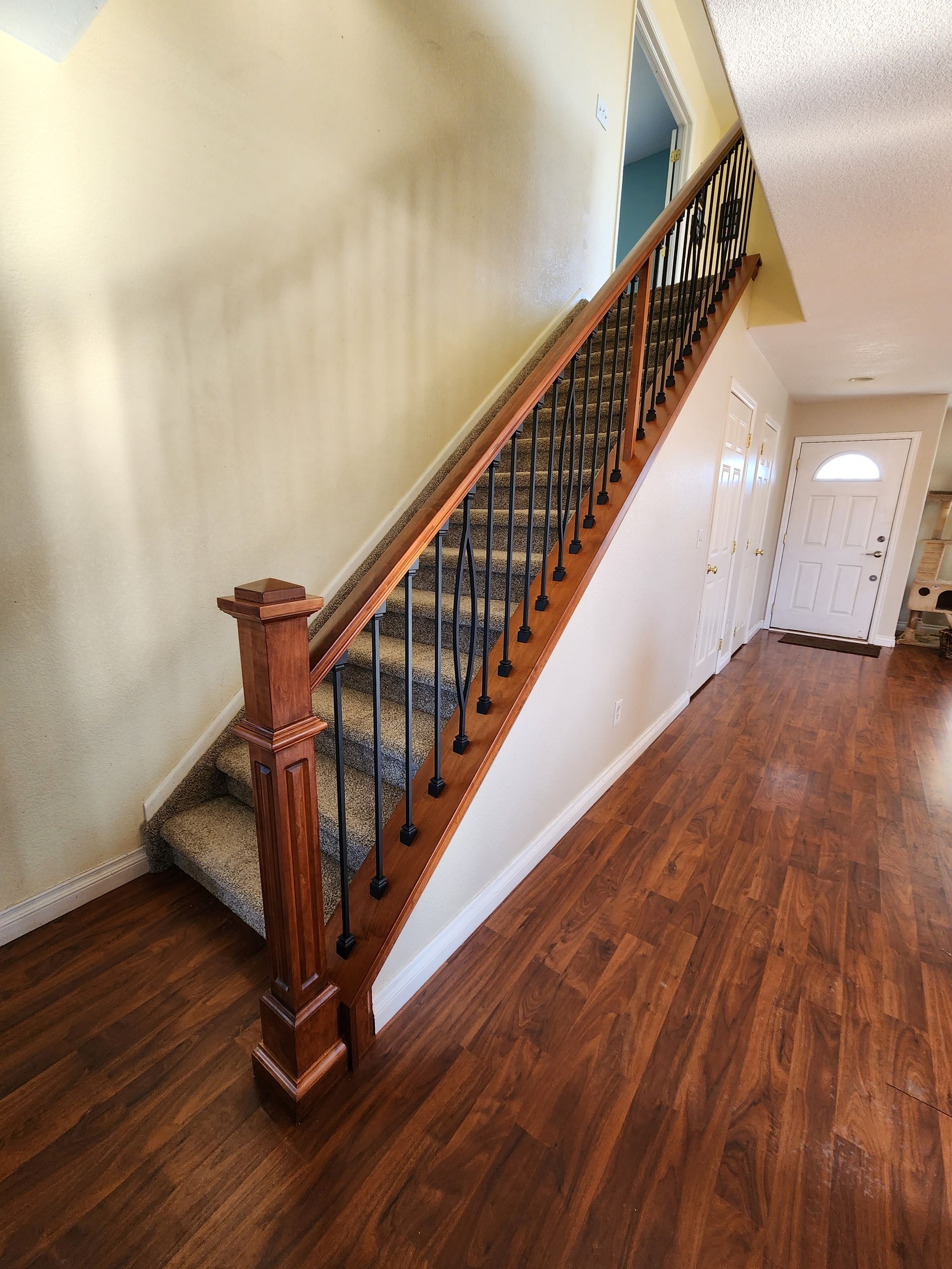 Wooden staircase with ornate black railing, carpeted steps, and hardwood floors.