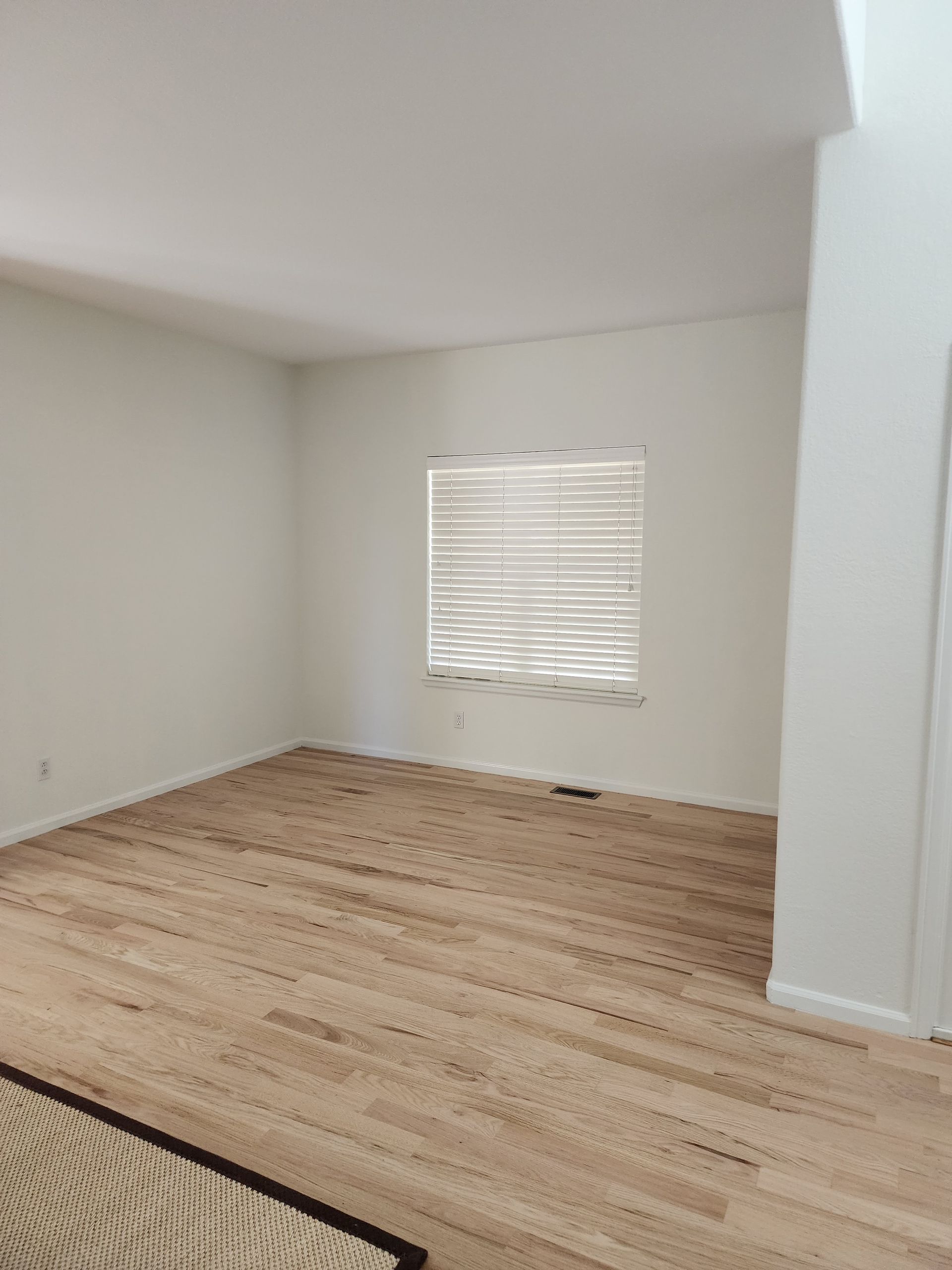 Empty room with hardwood floors, a window with blinds, and white walls.
