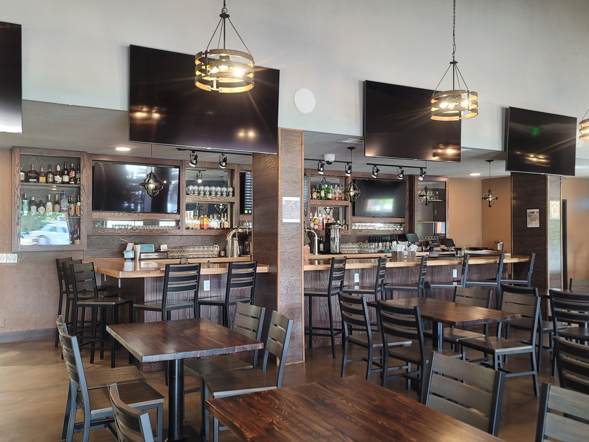 Interior of a bar with tables, chairs, and a long bar with stools. Multiple TVs are mounted on the wall.