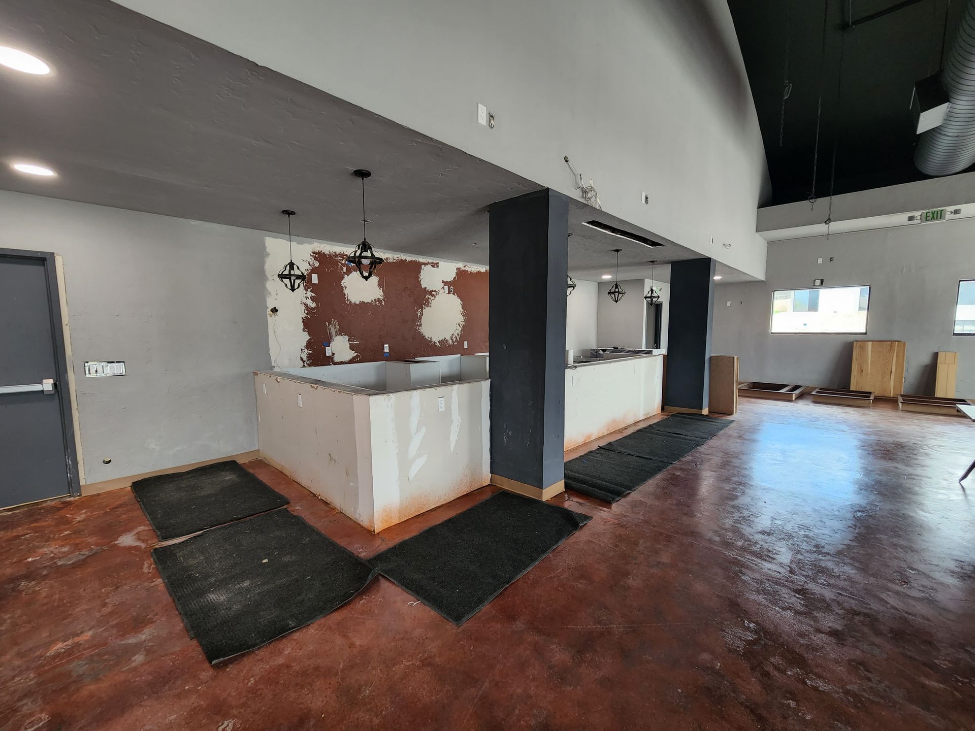 Empty office lobby with red wood floor, gray walls, and a white counter beneath a black beam.