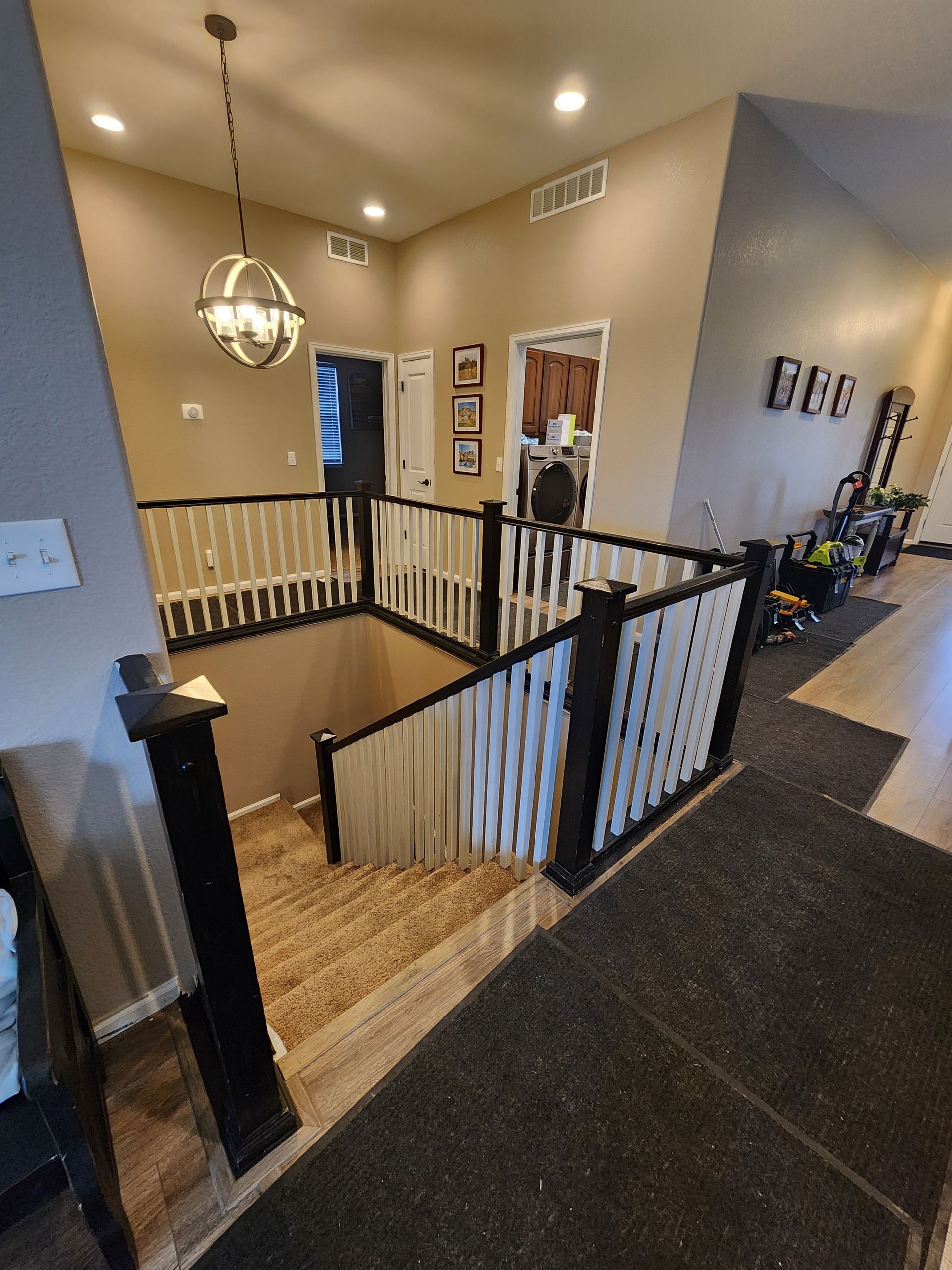 Staircase with black and white railing, leading to a second floor with doorways and decor. Wooden floor.
