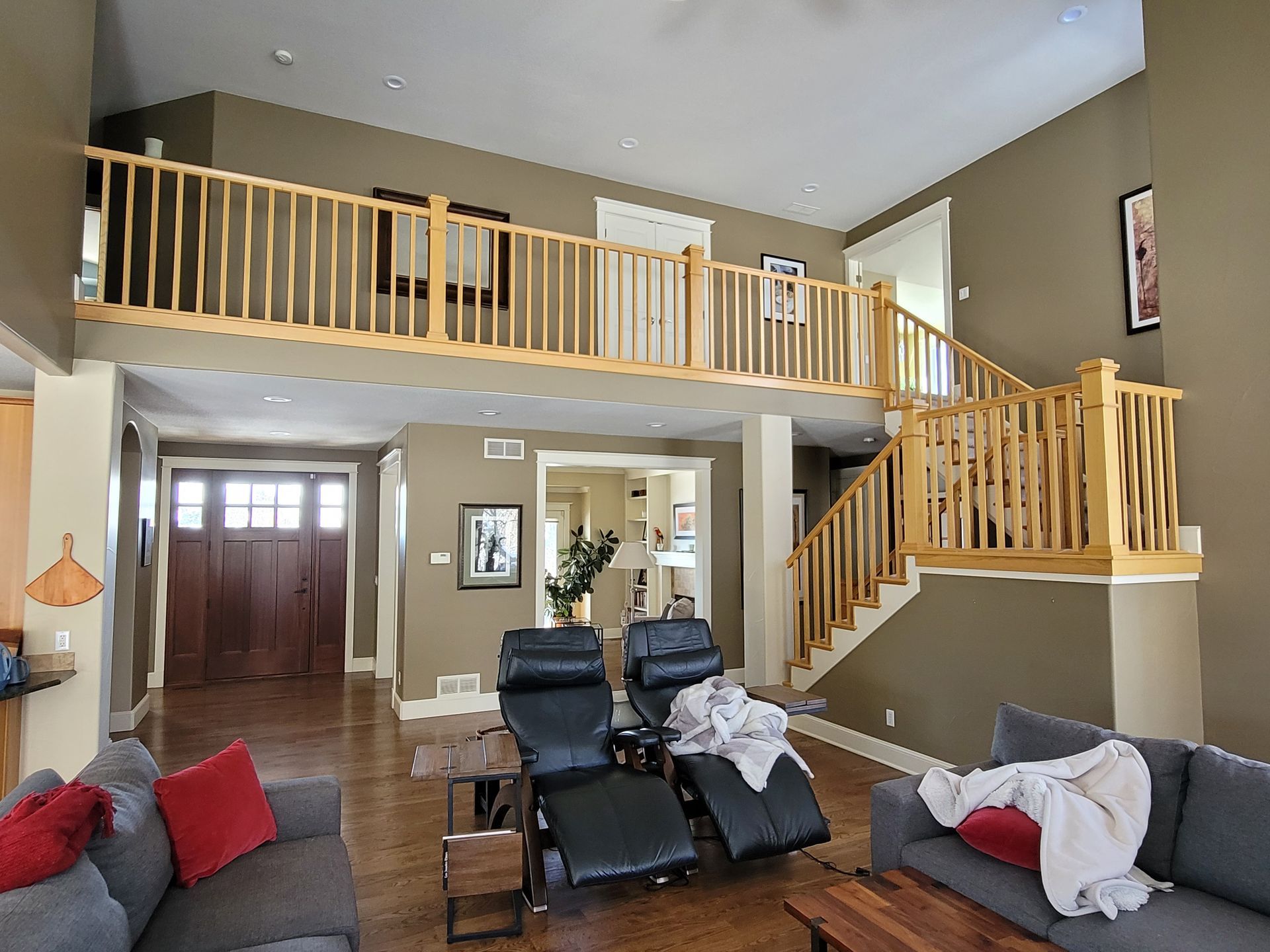Spacious living room with a loft and staircase, featuring a gray sofa, reclining chairs, and hardwood floors.