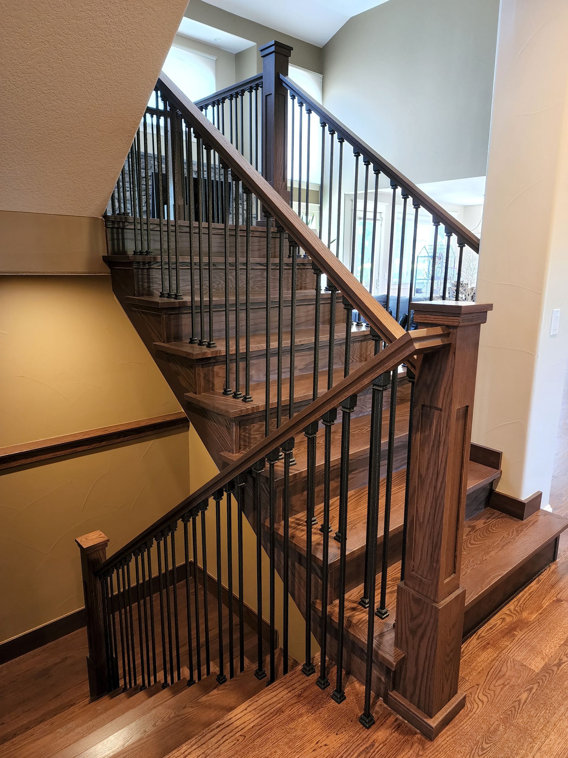 Wooden staircase with dark metal spindles and a stained wood finish.