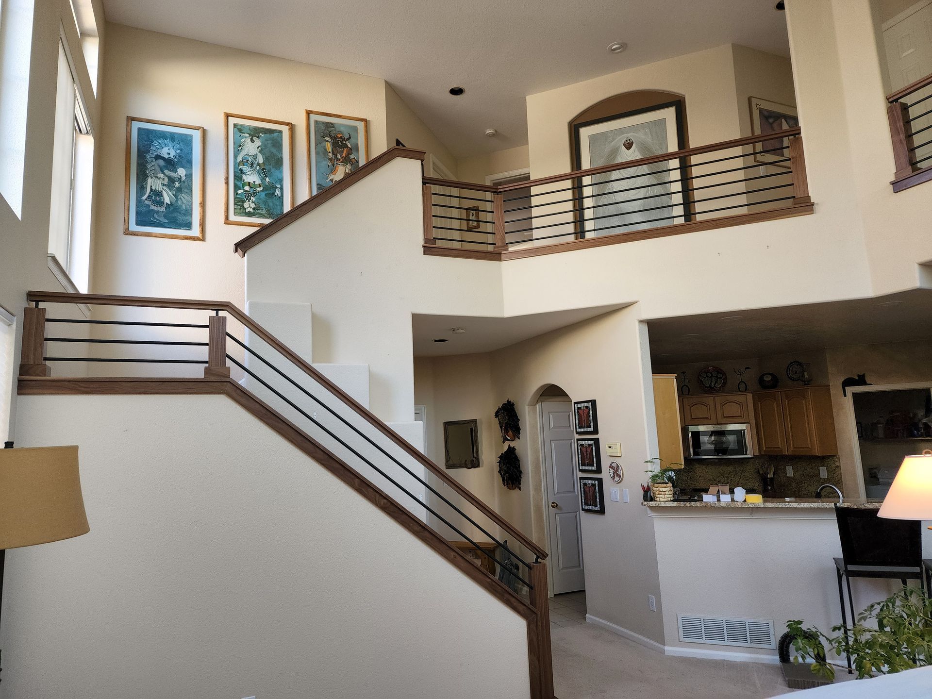 Two-story interior with staircase, paintings, and a view of the kitchen, featuring cream walls and wood accents.