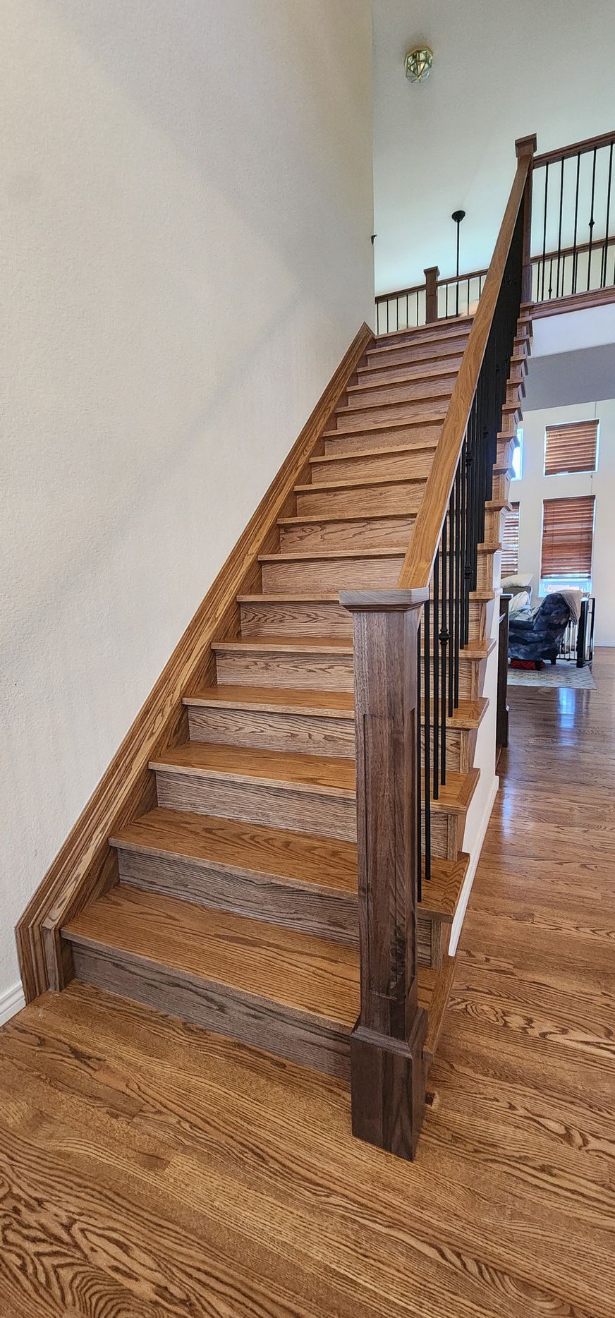 Wooden staircase with dark brown handrail and black iron spindles. Interior with light walls and wood floors.