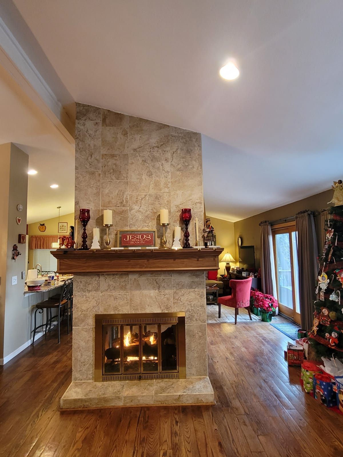 Fireplace with lit fire, wooden mantel, and candles, in a living room with wood flooring.