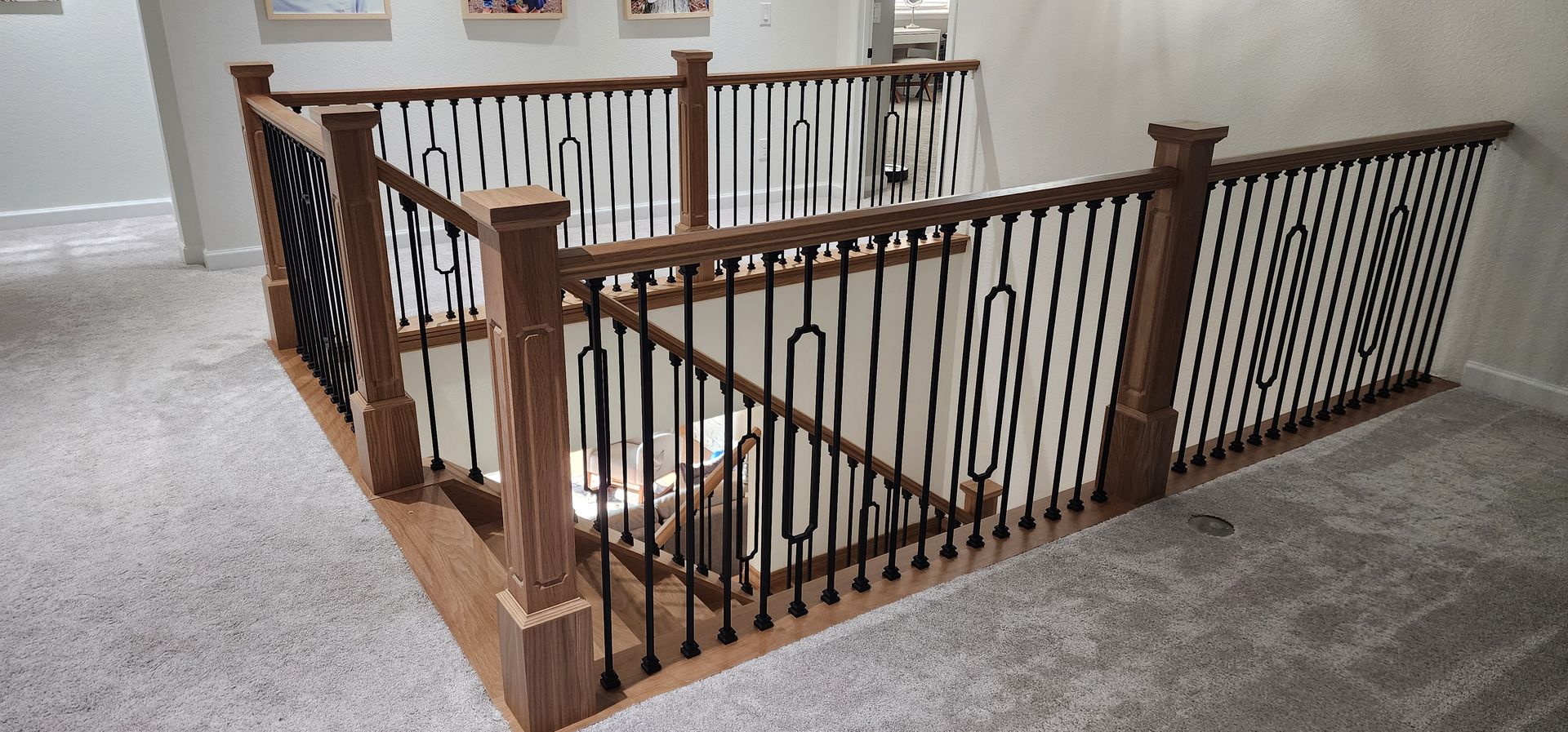 Staircase with wooden handrails and black metal balusters. Gray carpeted flooring.