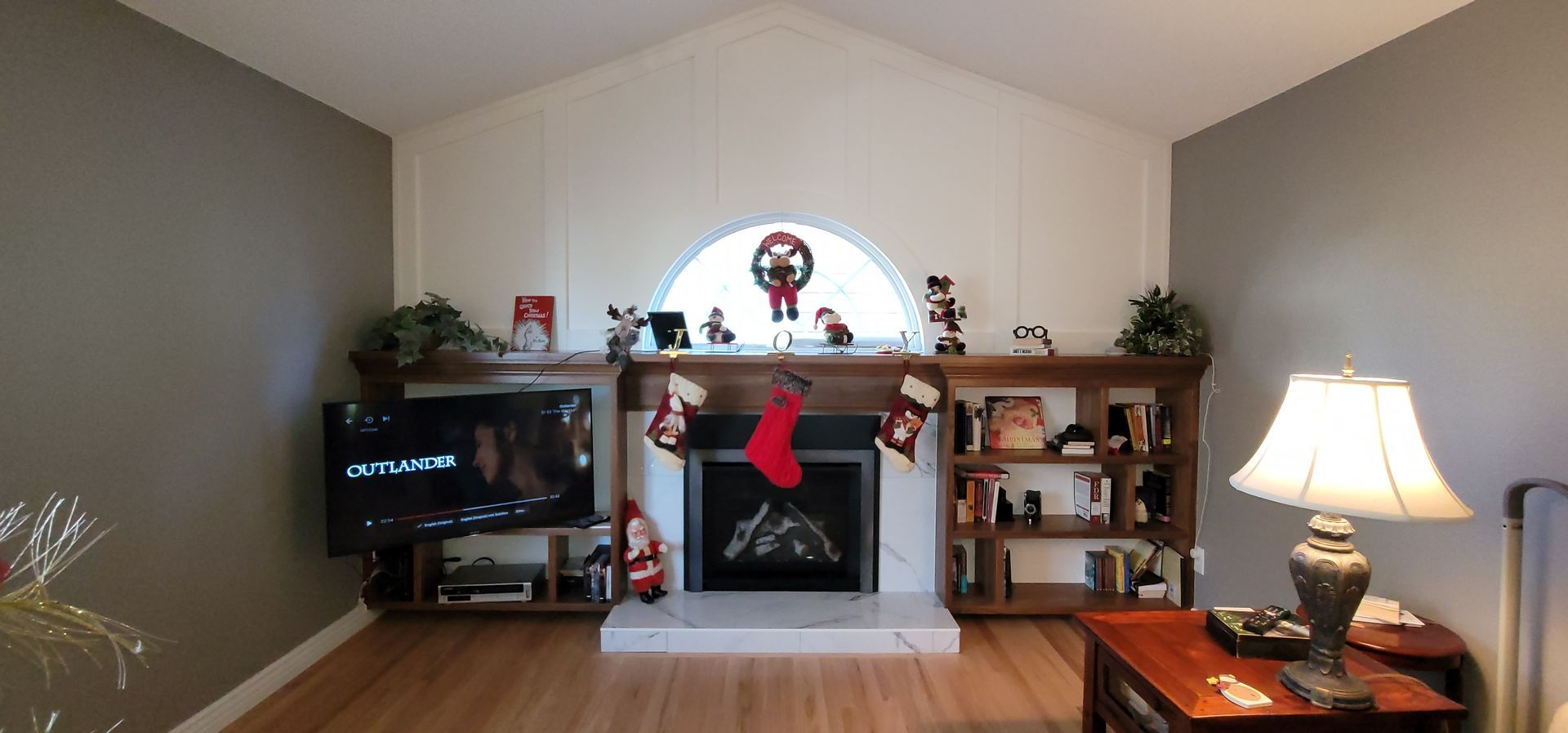 Living room with fireplace decorated for Christmas; TV, bookshelves, and a lamp.
