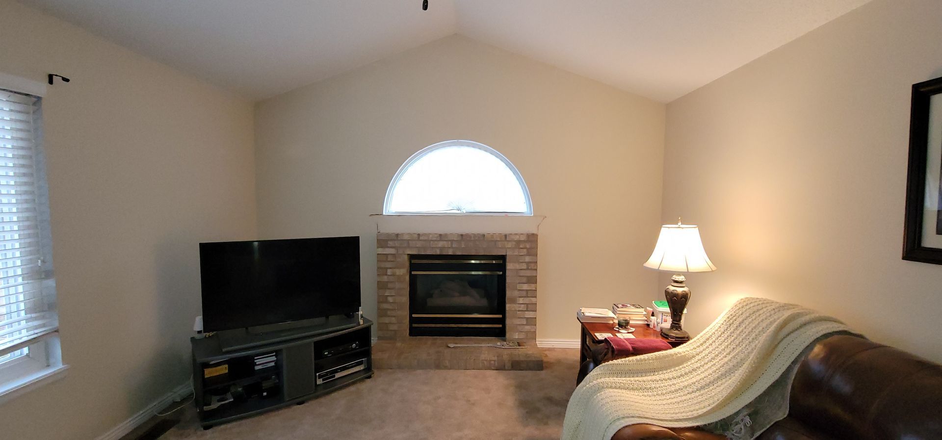 Living room with a fireplace, TV, and brown leather couch. Beige walls and vaulted ceiling.