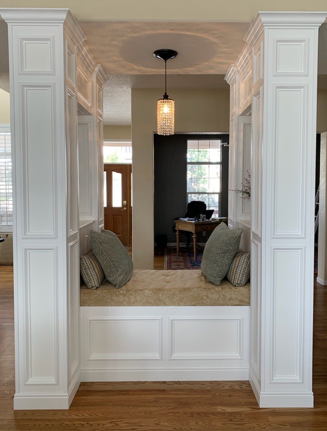 White built-in bench with pillows between two columns, centered in an entryway, and a hanging light above.