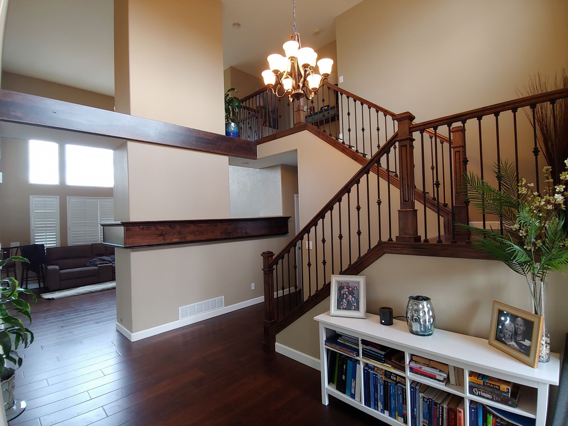 Interior view of a two-story foyer with staircase, hardwood floors, and a chandelier.