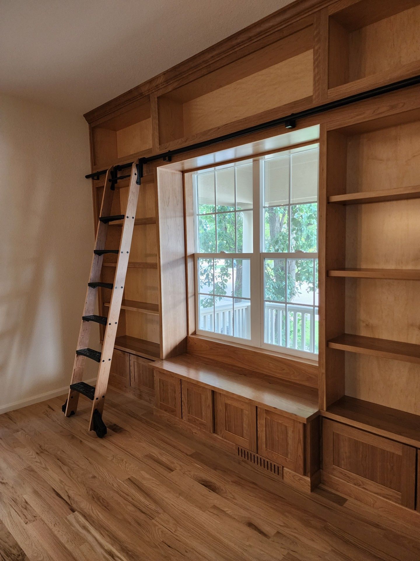 Wooden library with a window seat, built-in shelves, and a rolling ladder.