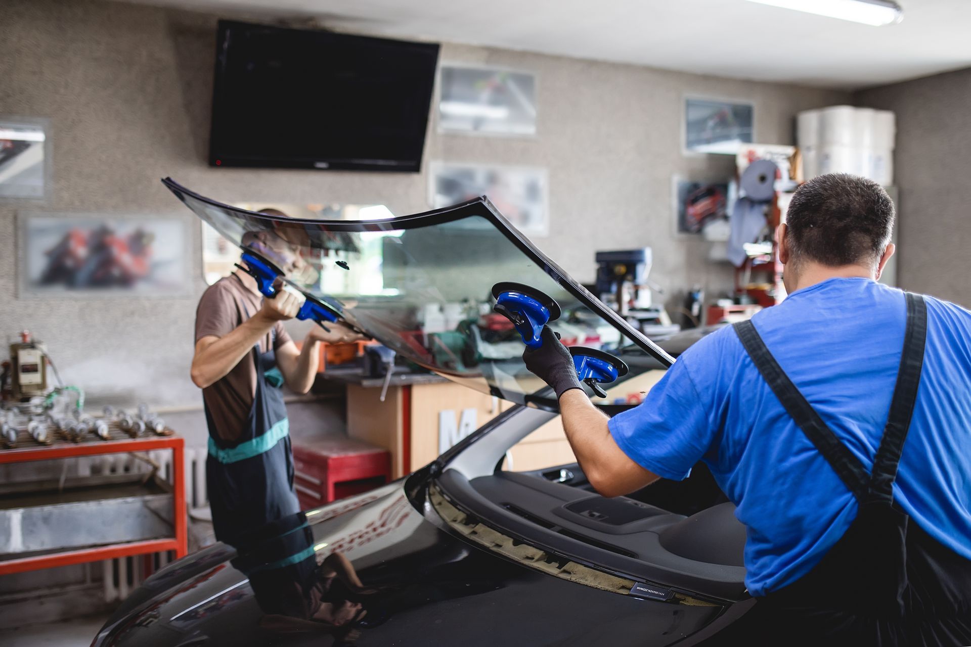 Technicians performing windshield replacement service in an auto glass shop