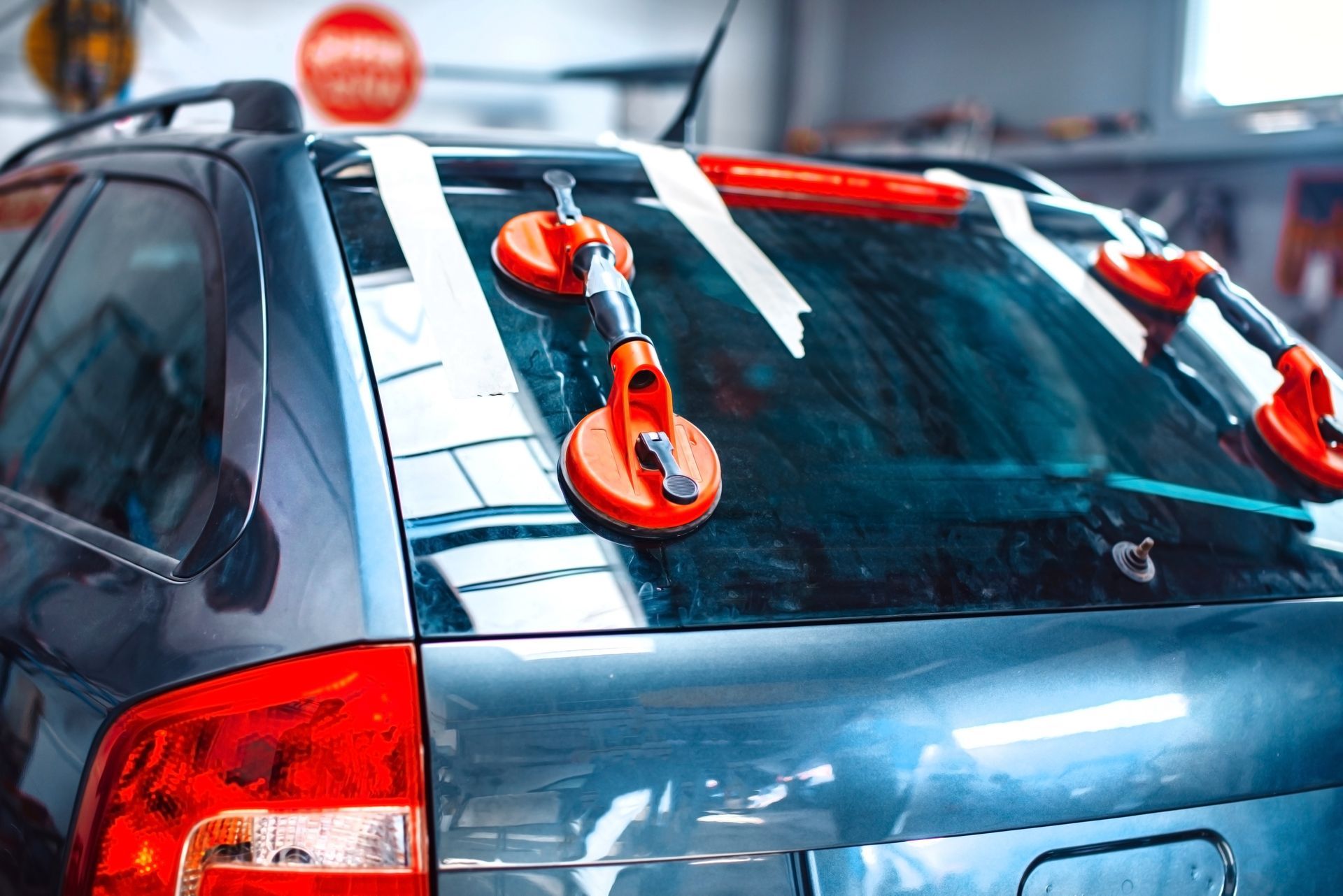 Blue car with orange suction cups attached to the roof and rear window in a garage-like setting