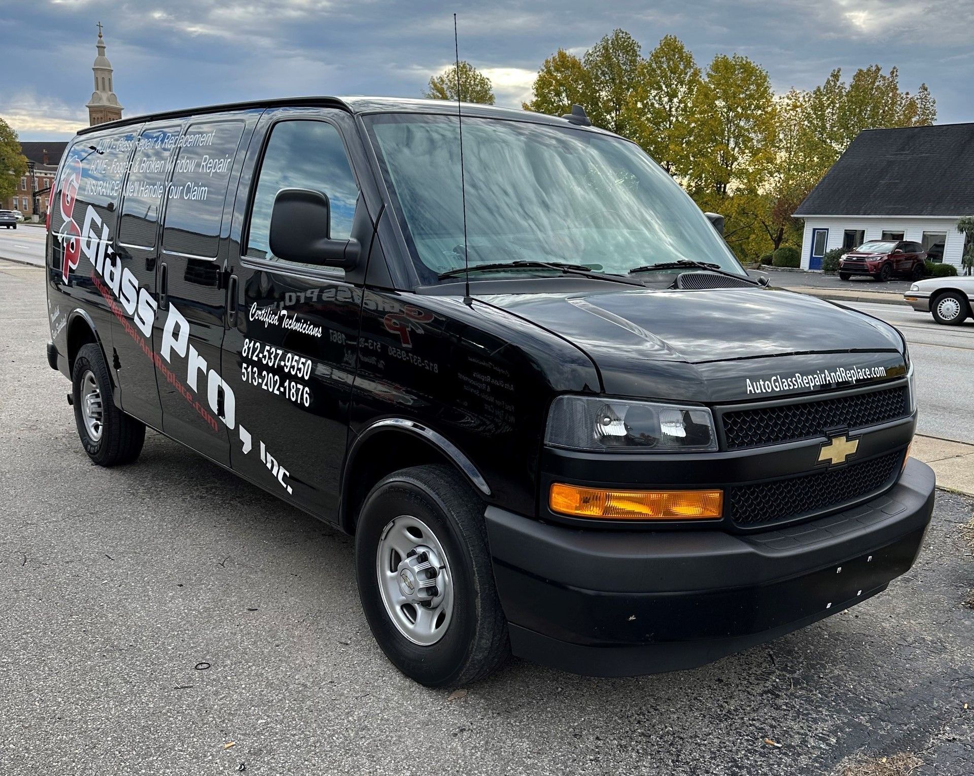 Black Chevrolet cargo van with company lettering parked on a street near houses and trees