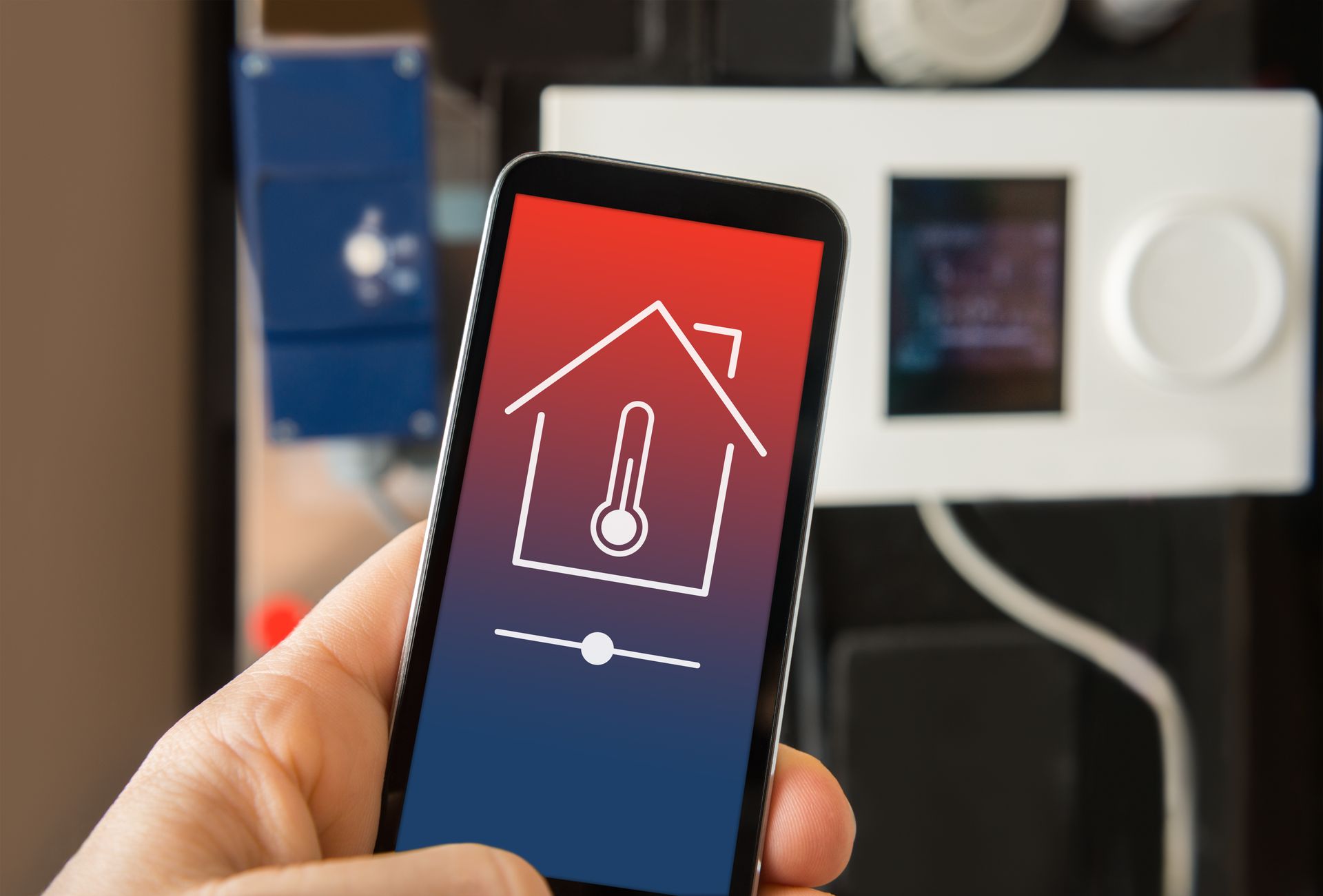A person is holding a smart phone with a house and a thermometer on the screen.