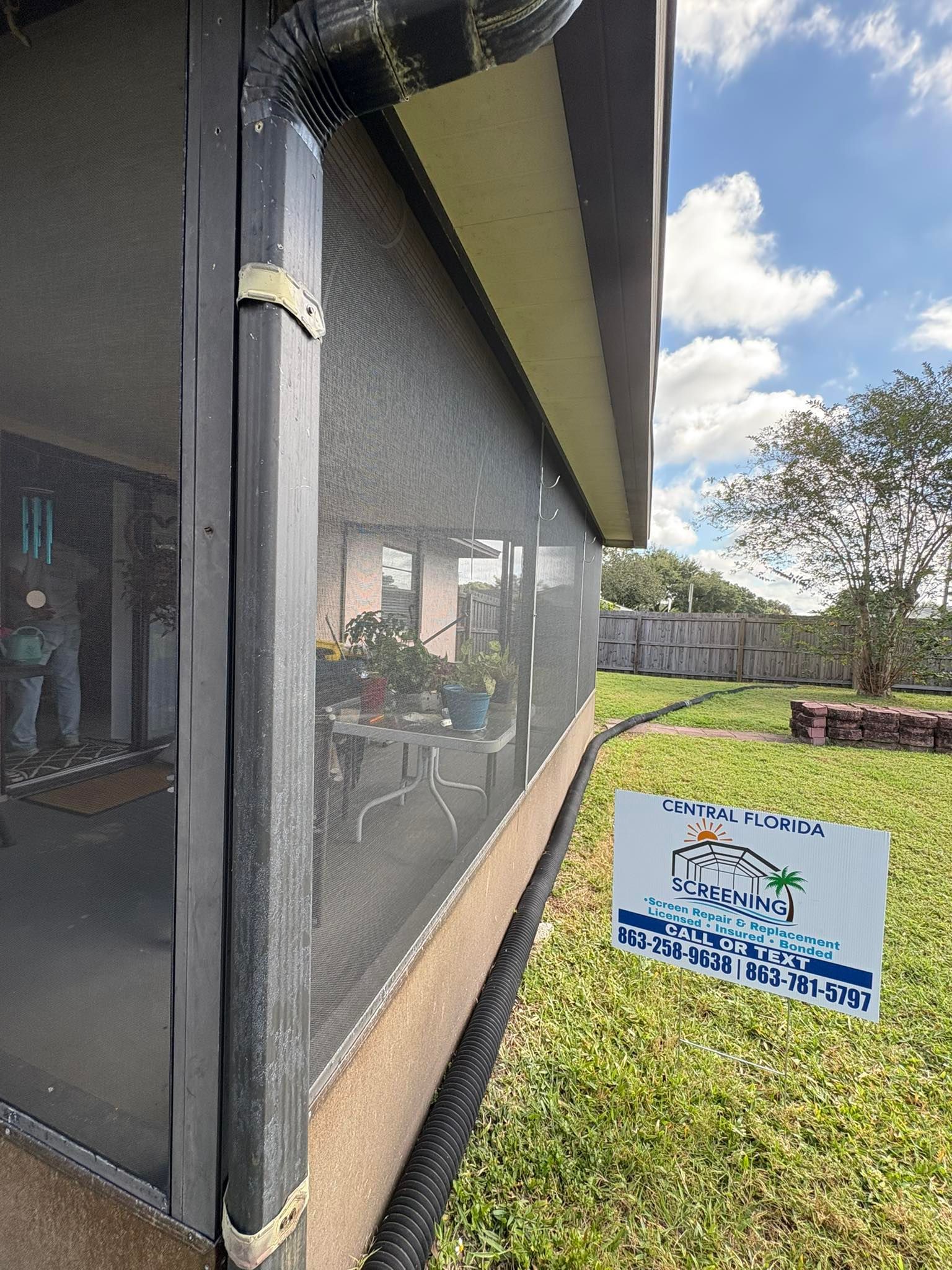 Screened-in porch with black frame, gutter, and a sign in the yard.